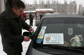 Водитель привязывает зеленую ленточку к зеркалу автомобиля