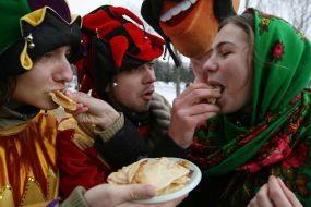 Участники празднования Масленицы кормят девушку блинами