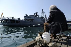 A fisherman looks at a frigate