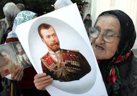 An elderly woman holds the portrait of Nikolay II