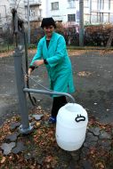 Женщина набирает в бидон воду