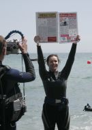 Journalists divers exhibit a newspaper, laid out under water