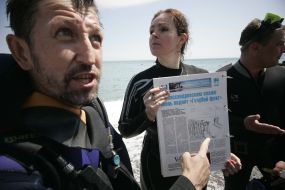 Journalists divers exhibit a newspaper, laid out under water
