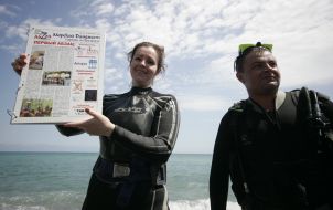 Journalists divers exhibit a newspaper, laid out under water