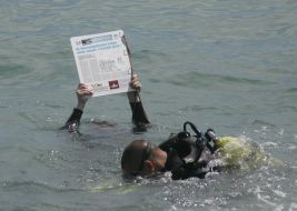 Journalists divers exhibit a newspaper, laid out under water