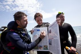Journalists divers exhibit a newspaper, laid out under water