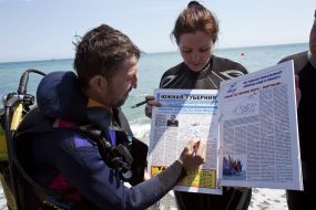 Journalists divers exhibit a newspaper, laid out under water