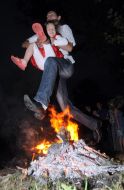 A young man with a little girl jumps over fire