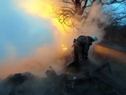 Пожарник осматривает крышу сгоревшего жилого дома