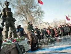 A man stands on knees near a monument to the warriors-afghans