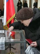 Пожилая женщина бросает бюллетень в урну для голования