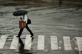 Мужчина под зонтиком переходит улицу