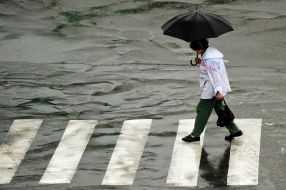 Женщина под зонтиком переходит улицу 