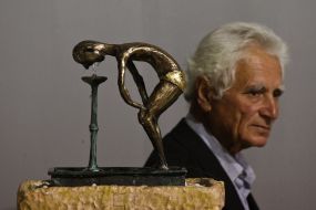 Мужчина возле инсталляции в виде человека, который пьет воду