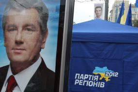 Агітаційний плакат із зображенням Віктора Ющенка біля намету Партії регіонів