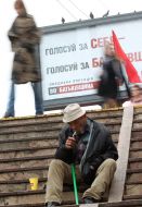 Бездомний підкурює цигарку на фоні агітаційного плакату ВО "Батьківщина"