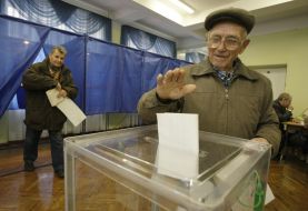 Пожилой мужчина бросает бюллетень для голосования в урну
