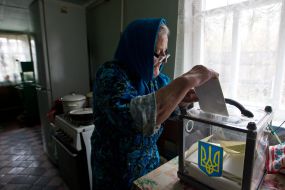 Пожилая женщина опускает бюллетень для голосования в урну