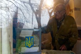 Пожилой мужчина опускает бюллетень для голосования в урну