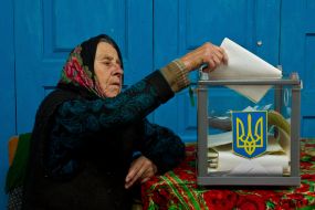 Пожилая женщина опускает бюллетень для голосования в урну