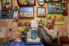 Пожилой мужчина опускает бюллетень для голосования в урну