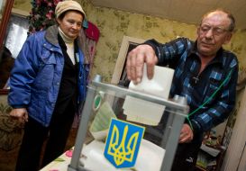 Пожилой мужчина опускает бюллетень для голосования в урну