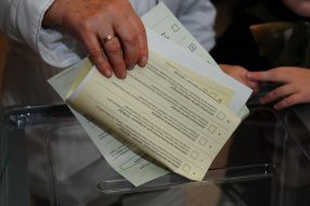 Женщина бросает бюллетени для голосования в урну