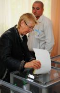 Женщина бросает бюллетени для голосования в урну
