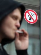 A young man smokes near the sign that prohibits smoking