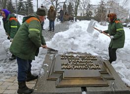 Работники коммунальных служб расчищают от снега мемориальную плиту 