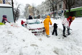 Дети и взрослые расчищают снег возле автомобиля