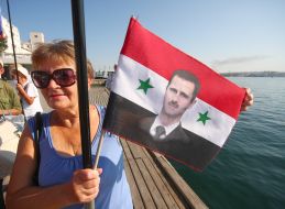 Жінка тримає в руках прапор із зображенням президента Сирії