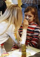 Жінка розмальовує дівчинці обличчя