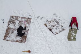 People clean carpets in the snow