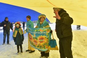 Люди стоять під величезним прапором України