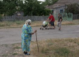 An elderly woman with a stick looks at passers-by