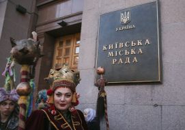 An actress in a theatrical costume on the background of a plaque bearing the inscription KMR