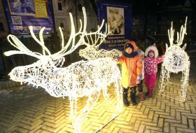 Children near voluminous figures of deer-garlands