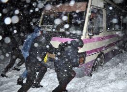 People are pushing a bus that is stuck on the road