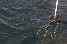 The priest lowered the cross into water