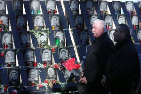 A man with a bouquet of carnations near the photos of the Heroes of Heavenly Hundred