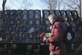 A man with a bouquet of carnations near the photos of the Heroes of Heavenly Hundred