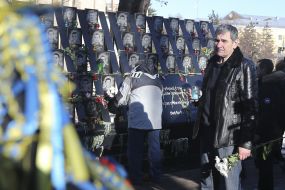 A man with a bouquet near the photos of the Heroes of Heavenly Hundred
