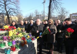 A man with a bouquet of carnations near the photos of the Heroes of Heavenly Hundred