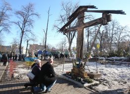 A man and a woman kneeling around the cross in honor of the Heroes of Heavenly Hundred