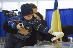A boy in the hands of a woman puts a ballot in a ballot box