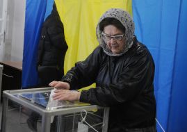 Літня жінка кидає бюлетень в скриньку