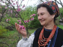 Woman in a Ukrainian costume near the flowering branch of a peach
