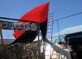 Мужчина устанавливает флаг УПА возле палатки