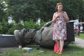 A woman stands near the tumbled bust of George Zhukov